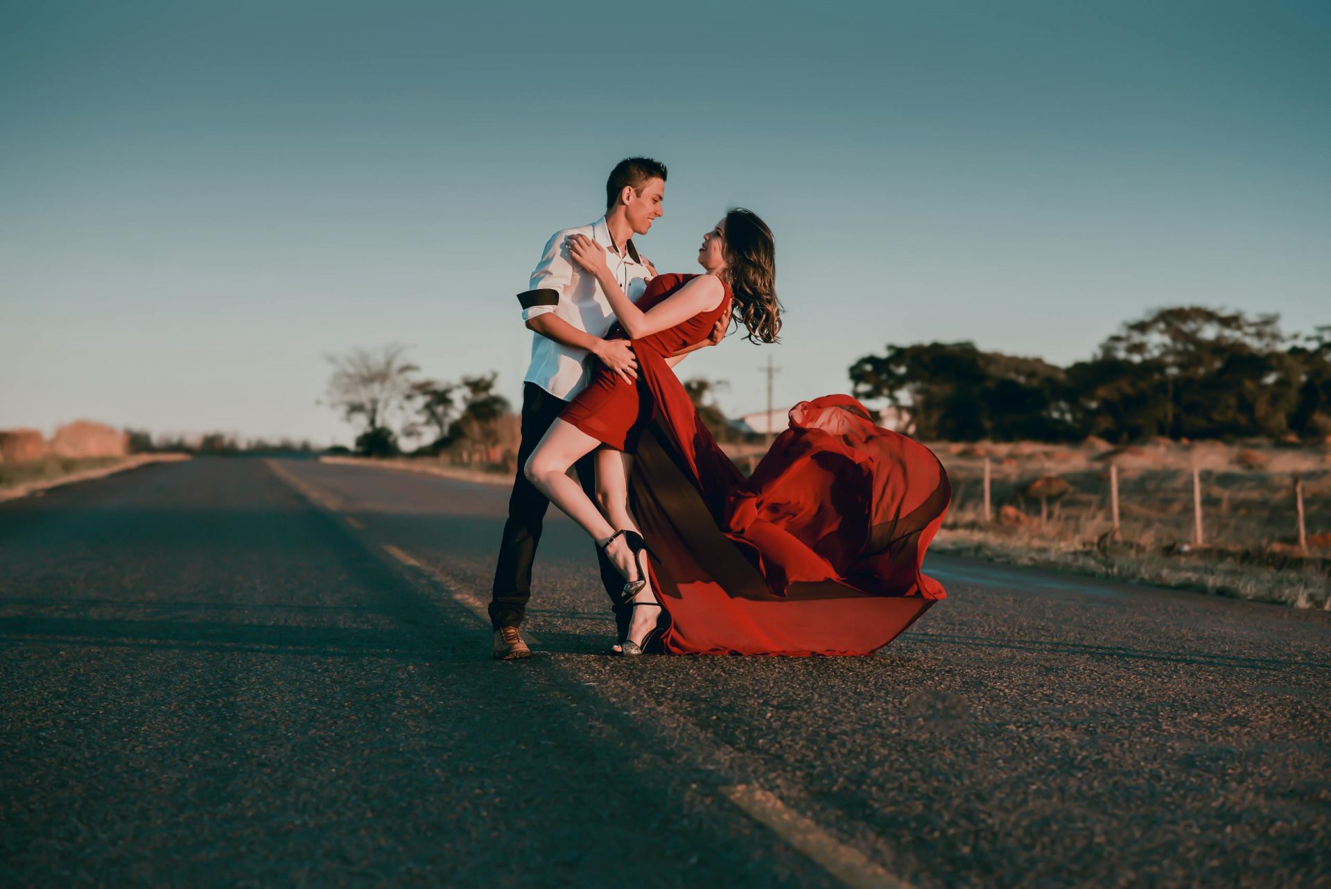 A couple in a passionate dance pose on an empty highway at sunset, showcasing love and romance.