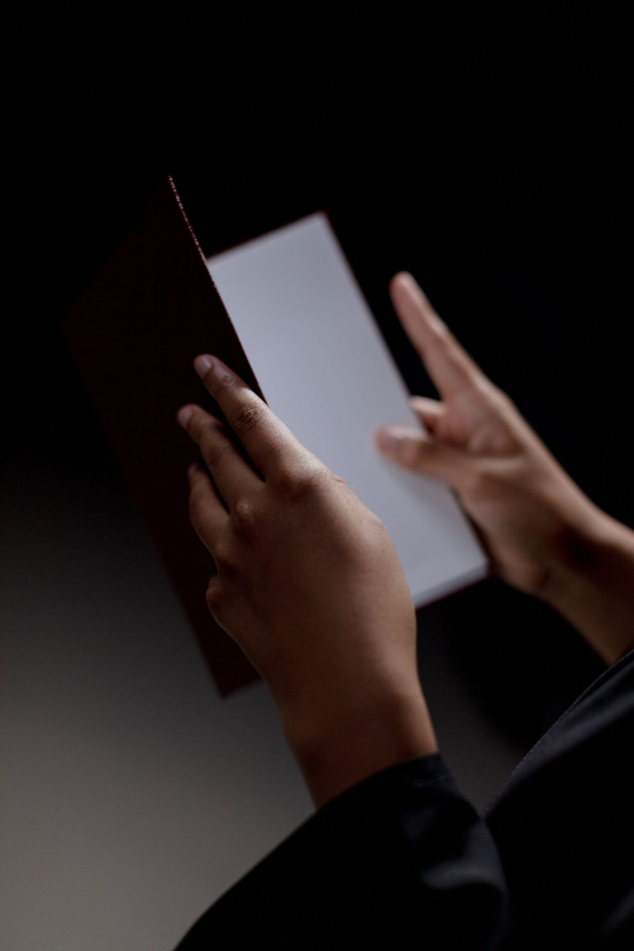 Unrecognizable person holding a diploma against a black background, symbolizing achievement and education.