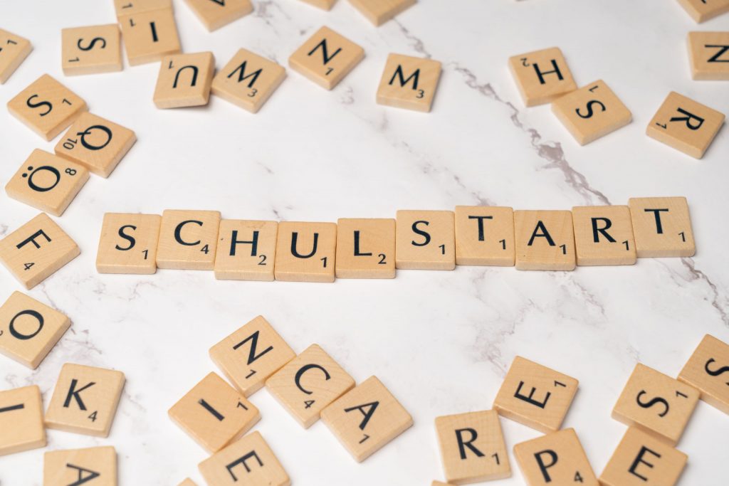 Wooden tiles forming the word 'Schulstart' on a marble surface, symbolizing school beginning.